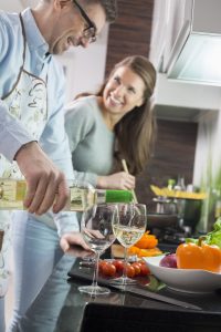 Man pouring white wine in glasses while cooking with woman at kitchen